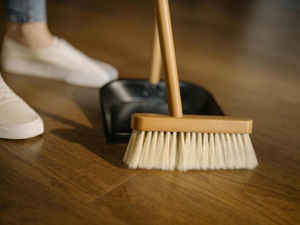 pexels-photo-4108711-4108711 Close-up of a broom and dustpan with white sneakers indoors, representing housekeeping and cleanliness.